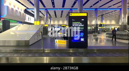 Les avertissements du gouvernement concernant Coronavirus dans le hall des bagages du terminal 2 de l'aéroport Heathrow de Londres le jour suivant que le premier ministre a déclaré que le Covid-19 « est la pire crise de santé publique d'une génération », et le plus grand scientifique du gouvernement a averti que jusqu'à 10 000 personnes au Royaume-Uni étaient déjà infectées. Banque D'Images