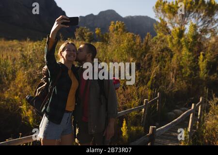 Vue de face de couple prenant des selfies sur un pont en bois Banque D'Images