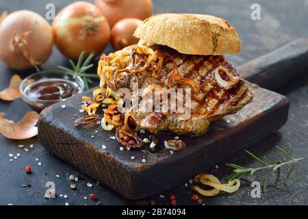 Gros sandwich à la viande : steak de filet de bœuf grillé avec rondelles d'oignons frits sur un rouleau frais Banque D'Images