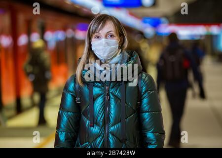 Femme en hiver manteau avec masque de protection sur le visage debout sur la station de métro, attendant le train, regardant inquiet. Mesures préventives Banque D'Images