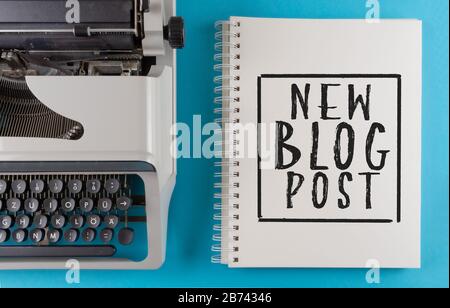 Texte NOUVEAU BLOG POST écrit sur le bloc-notes en spirale sur le bureau coloré avec ancienne machine à écrire, création de contenu et concept de blogging Banque D'Images