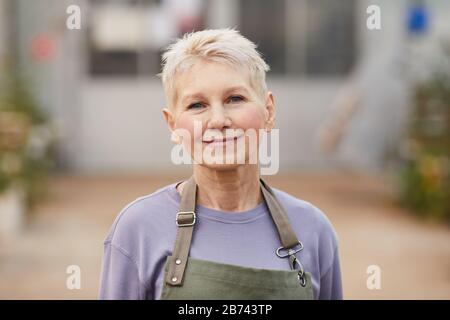Portrait d'une femme mûre avec des cheveux blonds courts regardant l'appareil photo tout en travaillant comme jardinier Banque D'Images