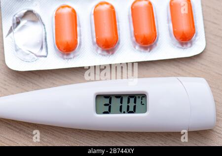 Thermomètre de gros plan indiquant une température élevée 37 et des pilules sur le tableau Banque D'Images