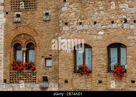 Geraniums rouges sur les fenêtres dans le centre historique de la ville médiévale perchée de San Gimignano, Toscane, Italie. Banque D'Images