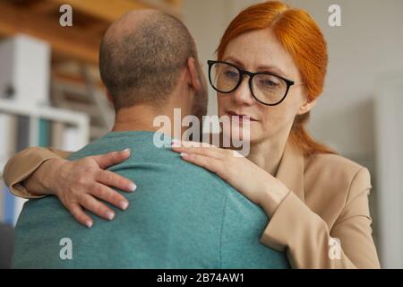 La jeune femme aux cheveux rouges sympathise avec un homme qu'elle embrasse et le soutient Banque D'Images