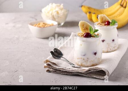 Muesli au miel croustillant de granola avec baies, banane, fromage cottage et yaourt naturel, un délicieux petit déjeuner sain, situé dans des pots en verre sur un Banque D'Images