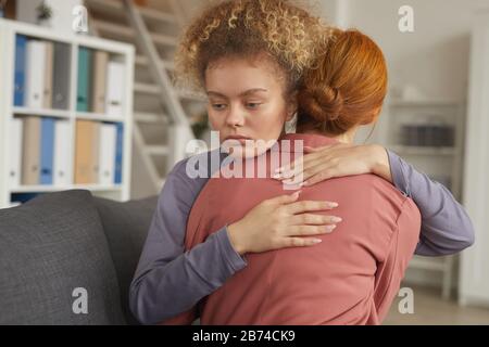 Jeune femme avec des cheveux bouclés embrassant et soutenant son ami pendant qu'ils assis sur un canapé dans la chambre Banque D'Images