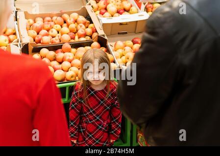 Une petite fille de 5 ans regarde mal à maman et papa. Bouleverser la fille hystérique avec des yeux fermés pleurant fort tout en manipulant les parents et se tenant contre la nourriture stalle dans le supermarché. Banque D'Images