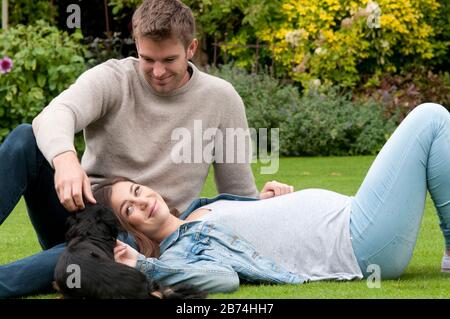 Belle jeune femme enceinte posée sur l'herbe avec son partenaire assis à côté d'elle Banque D'Images