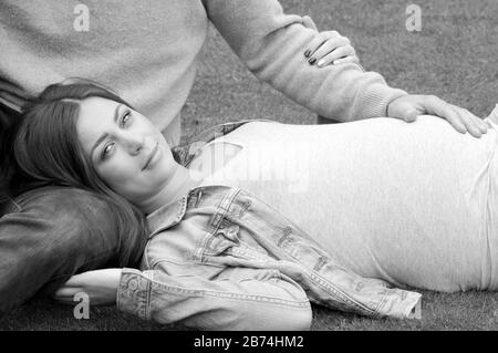 Noir et blanc, gros plan, belle jeune femme enceinte posée sur l'herbe avec son partenaire assis à côté d'elle Banque D'Images