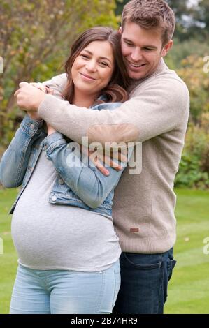 Belle jeune femme enceinte avec son partenaire la caresse dehors dans leur jardin Banque D'Images