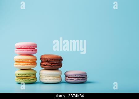 Les cookies macaroni de différentes couleurs sont disposés en forme de marches pyramidales sur un fond bleu. Espace libre. Le concept de minimalisme Banque D'Images