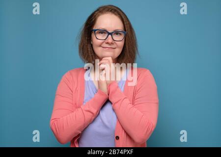 Belle et sûre d'elle-même femme d'âge moyen avec des lunettes souriant dans l'appareil photo sur le mur bleu. Émotion faciale positive. Banque D'Images