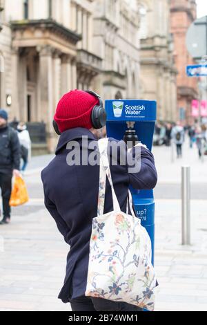 Personne utilisant le point de remplissage d'eau public - Scottish Water Top Tap - Buchanan Street, centre-ville de Glasgow, Ecosse, Royaume-Uni Banque D'Images