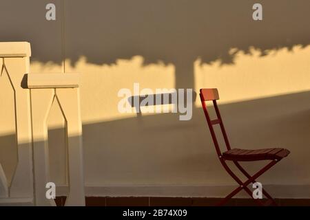 Table et chaise rouges dans le patio éclairé par la lumière du soir et l'ombre d'un arbre Banque D'Images