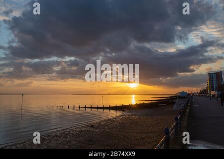 Southend-on-Sea, Royaume-Uni. 13 mars 2020. Coucher de soleil sur le front de mer de Southend, avec une lumière dorée reflétant l'estuaire de la Tamise. Promenade de l'Esplanade occidentale et groynes de plage visibles sous les nuages spectaculaires du soir. Penelope Barritt/Alamy Live News Banque D'Images