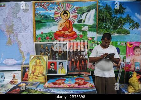 13.08.2014, Yangon, Myanmar, Asie - un commerçant de rue se tient devant son stand avec des affiches sur un marché de rue au centre de la ville et regarde son iPad. [traduction automatique] Banque D'Images