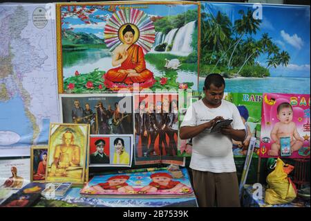 13.08.2014, Yangon, Myanmar, Asie - un commerçant de rue se tient devant son stand avec des affiches sur un marché de rue au centre de la ville et regarde son iPad. [traduction automatique] Banque D'Images