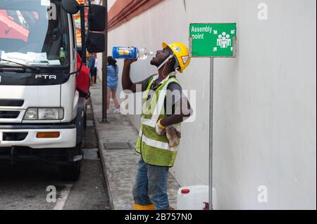 04.04.2018, Singapour, République de Singapour, Asie - un travailleur se tient au bord de la route à Chinatown pour boire de l'eau à partir d'une bouteille. [traduction automatique] Banque D'Images