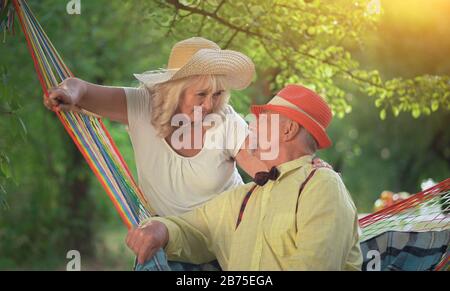 L'élégant homme est assis dans le Hammock coloré recouvert d'UN Blanket bleu.sa femme pend sur le Hammock.elle met sa main sur le Shou de l'homme Banque D'Images