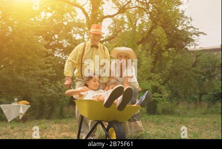 Le couple âgé pousse ses petits-enfants dans un Wheelbarrow.tous les membres de la famille sont très heureux.concept de vacances actives Banque D'Images