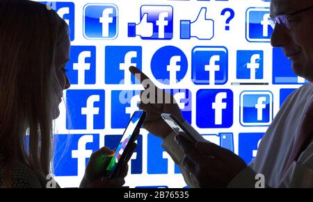 Les silhouettes d'une femme et d'un homme avec un smartphone entre leurs mains peuvent être vues devant le logo Facebook, le 12.01.2016. Illustration pour les amis Facebook. [traduction automatique] Banque D'Images
