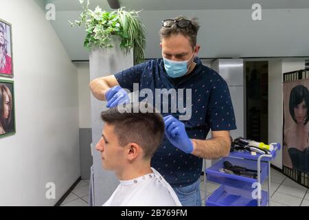 Ferrara, 13 Mars 2020. Un coiffeur travaille dans son salon de coiffure portant un masque de sécurité et des gants en raison de l'urgence du coronavirus à Ferrara, en Italie. Crédit: Filippo Rubin / Alay Live News Banque D'Images