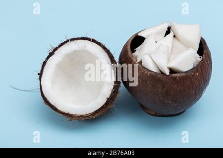 La moitié des morceaux de noix de coco et de noix de coco dans un vase en bois sur fond bleu. Banque D'Images