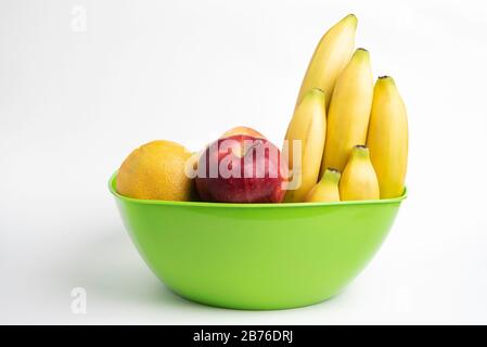 Un bol en plastique vert vif avec des fruits frais et mûrs disposés avec art, tels que des pommes, des bananes, des oranges et d'autres sur un fond blanc Uni. Banque D'Images