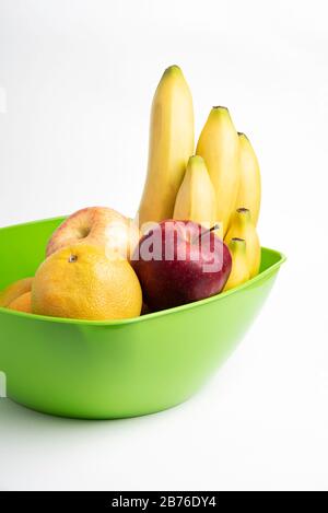 Un bol en plastique vert vif avec des fruits frais et mûrs disposés avec art, tels que des pommes, des bananes, des oranges et d'autres sur un fond blanc Uni. Banque D'Images