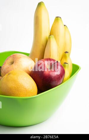 Un bol en plastique vert vif avec des fruits frais et mûrs disposés avec art, tels que des pommes, des bananes, des oranges et d'autres sur un fond blanc Uni. Banque D'Images