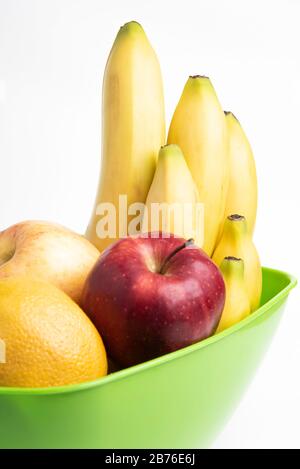 Un bol en plastique vert vif avec des fruits frais et mûrs disposés avec art, tels que des pommes, des bananes, des oranges et d'autres sur un fond blanc Uni. Banque D'Images
