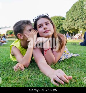 Un jeune gars chuchote dans l'oreille de la fille tout en allongé sur l'herbe verte . Banque D'Images