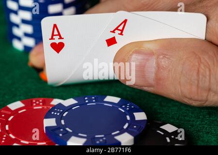 Une main caucasienne masculine montrant une paire d'As dans le trou, les coeurs et les diamants, un pont standard rouge et blanc de cartes avec des jetons bleus, rouges et noirs o Banque D'Images