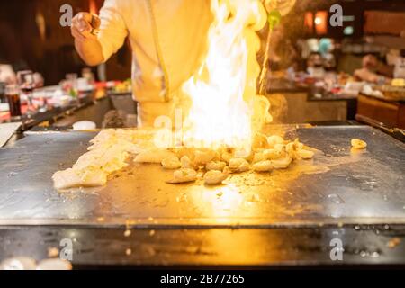 Le chef Teppanyaki prépare des fruits de mer japonais et des crevettes sur une plaque en métal chaud avec feu flamboyant. Banque D'Images