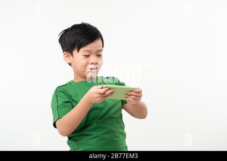 Portrait d'un mignon petit enfant satisfait de jouer aux jeux sur smartphone plus isolé sur fond blanc Banque D'Images