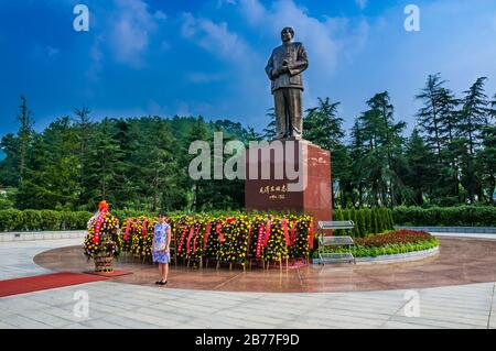 Une jeune fille chinoise dans une robe de style cheongsam pose pour une photo devant le bronze de six mètres de haut de la statue de Mao Zedong dans sa ville natale de Shaos Banque D'Images