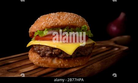 Vue rapprochée du délicieux hamburger de bœuf frais sur plateau en bois sur fond de table noir Banque D'Images