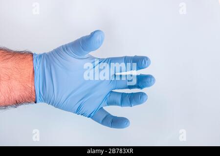 La main du médecin dans un gant médical bleu sur un fond bleu clair. Banque D'Images