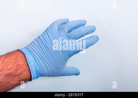 La main du médecin dans un gant médical bleu sur un fond bleu clair. Banque D'Images