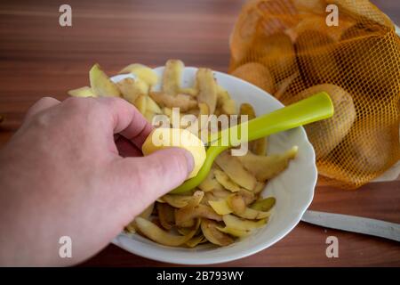 une petite pomme de terre pelée est maintenue d'une main sur un bol de pelure de pomme de terre Banque D'Images