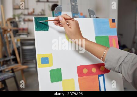 Main de la jeune étudiante féminine avec peinture de peinture vert foncé carré dans le coin supérieur gauche du papier à la leçon dans l'école d'arts Banque D'Images