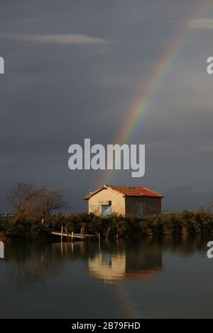 L'arc-en-ciel hivernal sur une hutte de pêcheur et son reflet sur le bord d'un chemin d'attelage (Salines, étangs de Villeneuve-lès-Maguelone, France) Banque D'Images