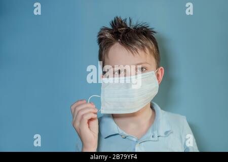 L'adolescent prend son masque médical sur fond bleu. Enfant avec grippe, grippe ou froid protégé contre les virus, pollution dans une mauvaise situation épidémique, amo Banque D'Images