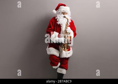 Père Noël jouant au saxophone et se penchant sur un mur gris clair Banque D'Images