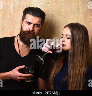 L'homme avec barbe et fille tient des boissons sur fond beige. Couple amoureux des verres à alcool à la date. Alcool et concept de fête. Petite amie et petit ami avec des visages délicats buvez du vin rouge et du cognac Banque D'Images