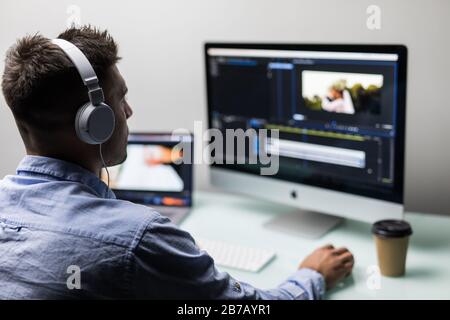 Jeune homme éditeur de vidéo avec travaille avec des films sur son ordinateur personnel avec grand écran au bureau Banque D'Images