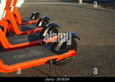 Quatre scooters électriques à bord d'un trottoir à Kohimarama, Auckland, Nouvelle-Zélande, louent de l'orange et de la neurone noire. Banque D'Images