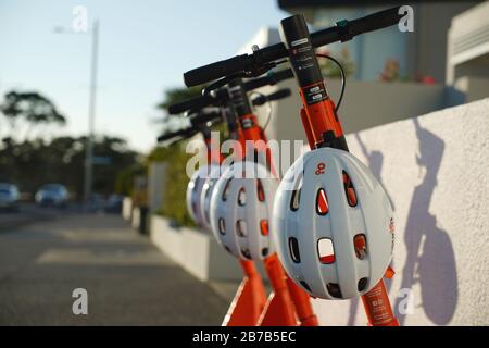 Quatre scooters électriques orange et noir à louer à bord d'un trottoir à Kohimarama, Auckland, Nouvelle-Zélande, avec casques de protection blancs. Banque D'Images