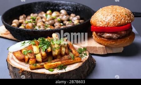 délicieux déjeuner rustique copieux. hamburger aux frites et champignons frits champignon en fonte sur les côtes de bois de la forêt sur fond gris gros plan Banque D'Images